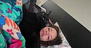 Spook is registered to the contest to win money with this photo: person, cat, bed, blanket, pillow, tattoo, black_cat, indoor, relaxing, cozy, floral, sleepwear, head, face, home, resting, comfort, animal, pet, casual