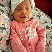 Reyli is registered to the contest to win money with this photo: baby, infant, pink_onesie, headband, bow, flower_pattern, cushion, sleepy, smile, child, cute, portrait, clothing, baby_girl, cozy, indoors, young_child, face, small_hands, soft_fabric