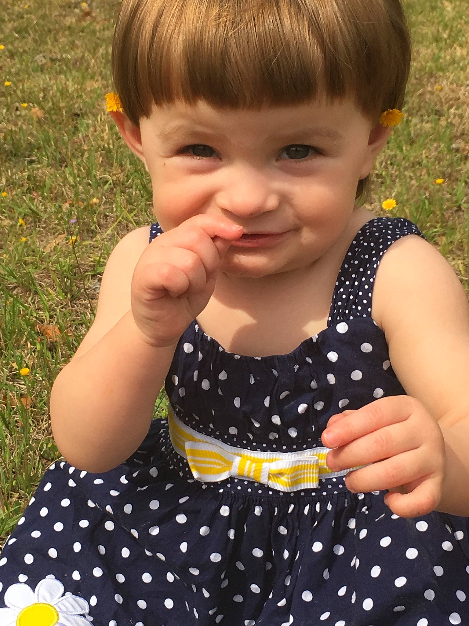 Delta is registered to the contest to win money with this photo: baby, baby_toddler_clothing, brown_hair, child, design, dress, finger, gesture, grass, hair, hairstyle, hand, pattern, person, play, polka_dot, skin, smile, summer, toddler