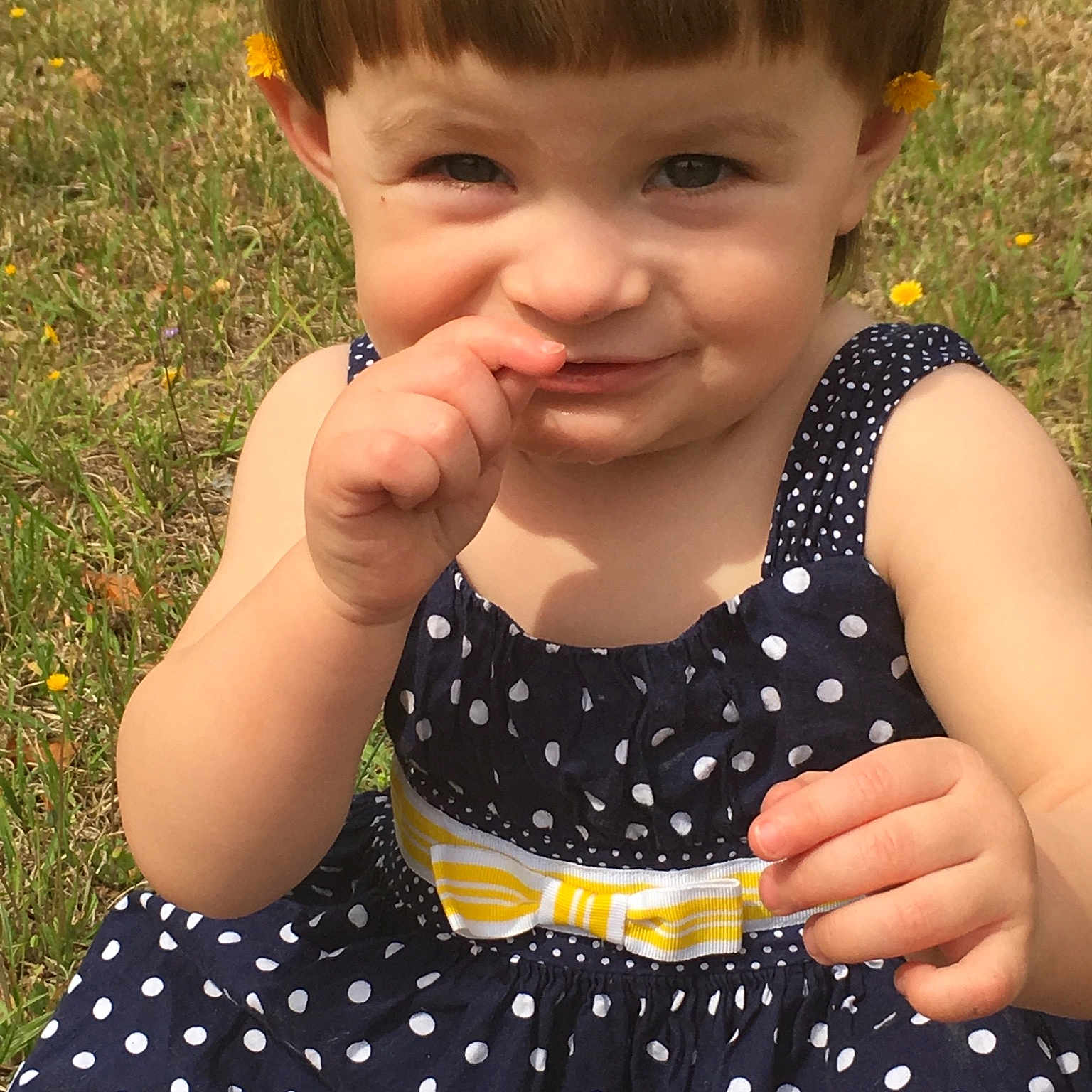 Delta is registered to the contest to win money with this photo: baby, baby_toddler_clothing, brown_hair, child, design, dress, finger, gesture, grass, hair, hairstyle, hand, pattern, person, play, polka_dot, skin, smile, summer, toddler