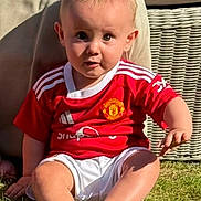 Ruben joined the competition — help win amazing prizes! baby, child, grass, outdoor, sitting, red_jersey, manchester_united, curious, sunlight, wicker_chair, cushion, barefoot, shorts, person, casual_clothing, summer, portrait, cute, young_child, daylight