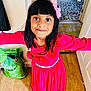 Mifraa is registered to the contest to win money with this photo: child, girl, pink_dress, headband, smiling, indoors, wooden_floor, flower, long_sleeves, person, happy, black_hair, fringe, carpet, doorway, household_item, bag, rice, patterned_rug, looking_at_camera