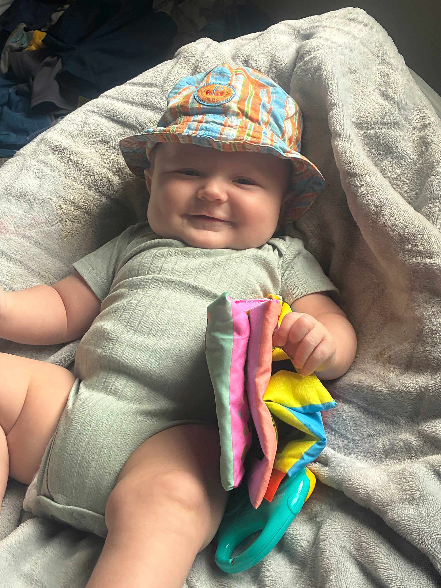 Hudson is registered to the contest to win money with this photo: baby, infant, hat, striped_hat, colorful, toy, blanket, drool, smile, chubby_cheeks, clothing, onesie, soft_texture, indoor, cute, child, playful, relaxed, happy, person