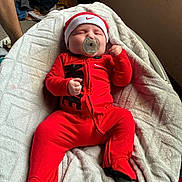 Hudson joined the competition — help win amazing prizes! baby, infant, pacifier, red_clothing, nike_logo, blanket, bed, sleeping, fist, footed_pajamas, hat, indoors, person, cute, newborn, soft_texture, relaxation, cozy, peaceful, lying_down