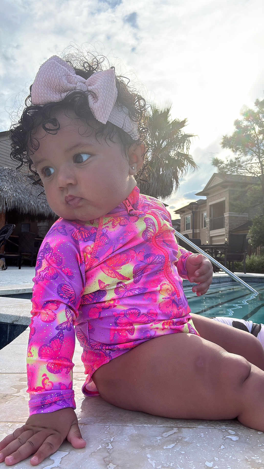 Aslhey Melanie joined the competition — help win amazing prizes! toddler, child, swimsuit, bow, curly_hair, poolside, water, outdoor, sunlight, sky, clouds, palm_tree, residential, hand, legs, face, earrings, colorful_clothing, marble_floor, summer