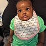Walonii is registered to the contest to win money with this photo: baby, infant, child, green_clothing, pink_headband, bib, love_pattern, sitting, indoor, closeup, cute, adorable, face, expression, diaper, person, headwear, black_background, soft_texture, curious_eyes
