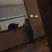 Midnight joined the competition — help win amazing prizes! toddler, cat, window, pajamas, indoor, wooden_floor, child, black_cat, curious, standing, windowsill, light, home, floor, animal, pet, baby, cozy, emojis, wall