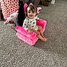 toddler, child, pink_chair, plush_chair, pillow, carpet, living_room, toy, smiling, cute, indoors, person, furniture, colorful, happy, seat, cozy, pattern, hair, face