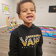 Liam joined the competition — help win amazing prizes! child, smiling, curly_hair, hoodie, vans_logo, playroom, toys, colorful, educational_poster, wooden_floor, happy, indoor, young_kid, casual_clothing, portrait, boy, floor_mat, television, wall_art, bright_lighting