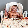 Maia is registered to the contest to win money with this photo: baby, high_chair, messy, food, smiling, face, child, indoor, happy, arm, table, feeding, skin, seat, cute, dirt, playful, infant, meal, expression