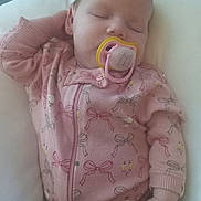 Maia is registered to the contest to win money with this photo: baby, sleeping, pacifier, pink_onesie, bows_pattern, cushion, relaxed, infant, child, peaceful, resting, hand, face, closed_eyes, indoor, soft_lighting, cute, cozy, portrait, person