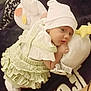 baby, infant, plush_toy, hat, green_dress, white_shirt, blanket, cuddling, lying_down, cute, soft_toy, child, indoors, comfort, sleepwear, face, small_hands, expression, cozy, resting