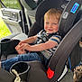 toddler, child, car_seat, car_interior, seatbelt, pacifier, smile, striped_shirt, jeans, holding_foot, window, door, greenery, daylight, happy, cute, safety, playful, indoors, person