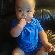 Calvin joined the competition — help win amazing prizes! baby, child, blue_clothing, sitting, finger_in_mouth, curious, leather_couch, indoors, infant, portrait, cute, chubby, young_child, casual, one_person, human, skin, short_hair, seated, expression