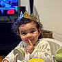 Alya a rejoint le concours — aidez-le/la à gagner de superbes lots ! toddler, child, crown, high_chair, toy, finger_on_lips, curly_hair, indoor, playful, cute, face, smile, clothing, furniture, person, young_child, baby_toy, expression, portrait, home