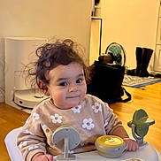 Alya a rejoint le concours — aidez-le/la à gagner de superbes lots ! toddler, baby_walker, child, indoor, curly_hair, flower_pattern, sweater, toy, smile, face, hand, wooden_floor, boots, fan, rug, furniture, home, person, play, cute