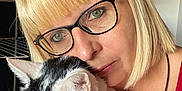 Isidore participe au concours pour gagner de l'argent avec cette photo : woman, cat, glasses, blonde_hair, indoor, close_up, pet, holding, face, yellow_eyes, red_clothing, ring, whiskers, short_hair, portrait, human, animal, domestic_cat, calm, cozy