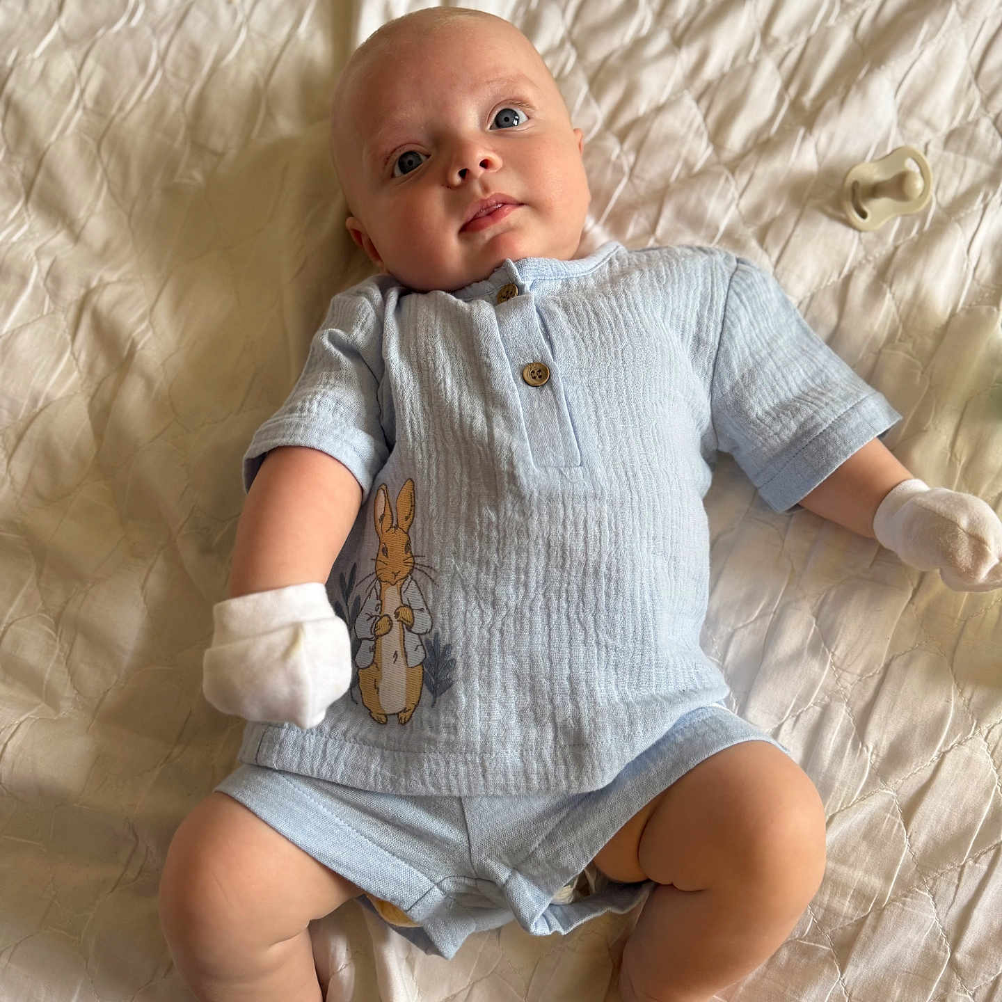 Marley is registered to the contest to win money with this photo: baby, blanket, blue_clothing, bunny_print, child, cute, expression, face, feet, head, indoor, infant, legs, lying_down, mittens, newborn, pacifier, person, skin, soft_light