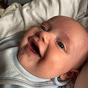 Marley is registered to the contest to win money with this photo: baby, smiling, close_up, blue_eyes, infant, cute, happy, face, skin, mouth, cheeks, ear, clothing, blanket, soft, laying_down, portrait, child, indoor, light