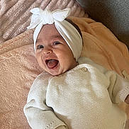 Lyna participe au concours pour gagner de l'argent avec cette photo : baby, blanket, child, couch, cozy, cute, face, happy, headband, indoor, infant, knitted_clothing, lying_down, person, portrait, relaxed, smiling, soft_texture, toddler, white_clothing