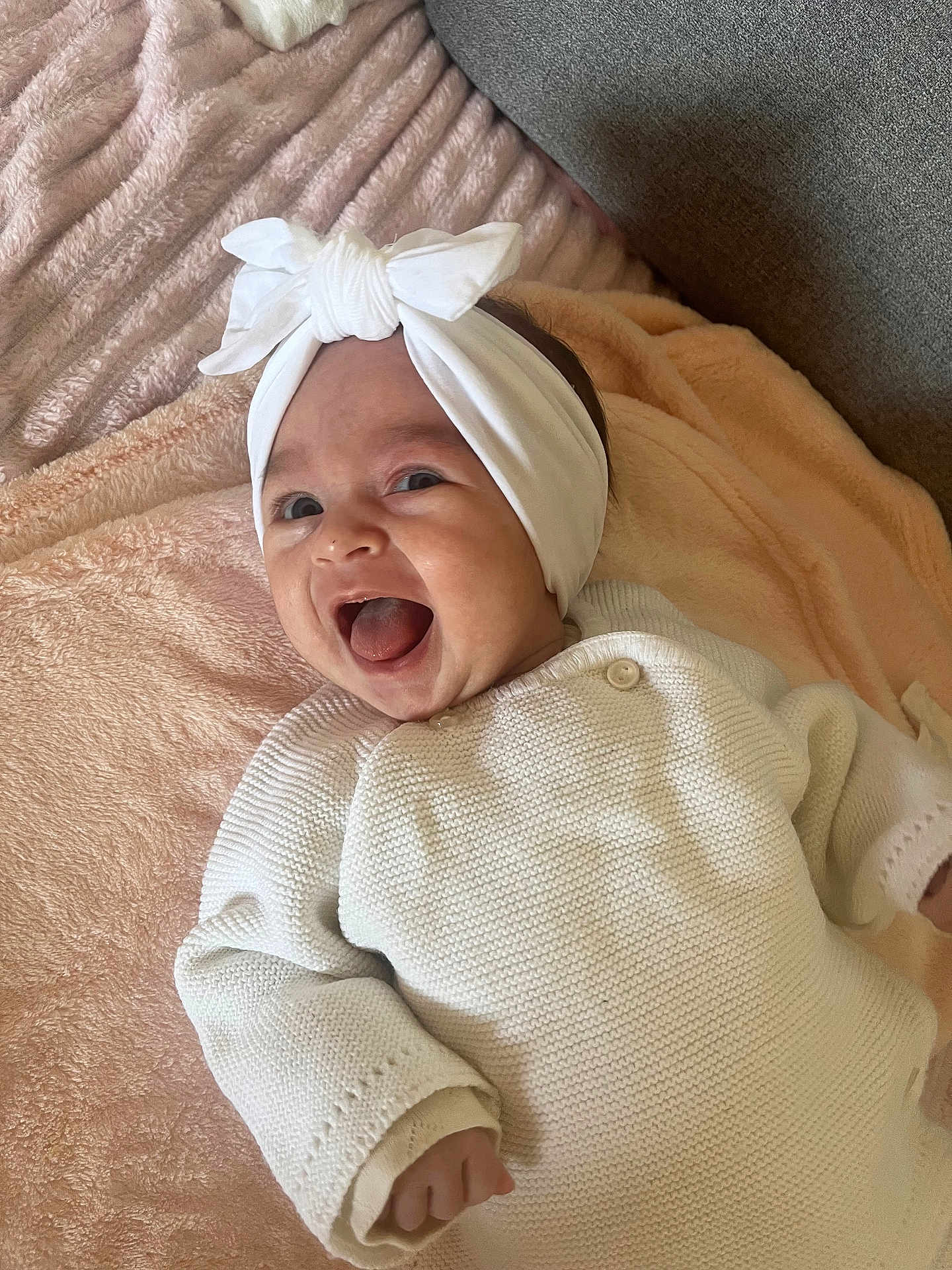 Lyna participe au concours pour gagner de l'argent avec cette photo : baby, blanket, child, couch, cozy, cute, face, happy, headband, indoor, infant, knitted_clothing, lying_down, person, portrait, relaxed, smiling, soft_texture, toddler, white_clothing