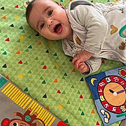 Ambre participe au concours pour gagner de l'argent avec cette photo : baby, child, play_mat, toy, smiling, happy, infant, colorful, pattern, face, clothing, indoor, cute, lying_down, hand, head, expression, playtime, monkey_toy, ball_toy