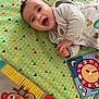 baby, child, play_mat, toy, smiling, happy, infant, colorful, pattern, face, clothing, indoor, cute, lying_down, hand, head, expression, playtime, monkey_toy, ball_toy