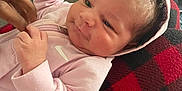 Nova is registered to the contest to win money with this photo: baby, blanket, checkered_pattern, closeup, clothing, comfort, couch, curly_hair, expression, face, hand, indoor, infant, person, pink_hoodie, red_and_black, relaxation, sleeve, soft_texture, water_bottle