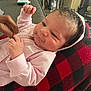 Nova is registered to the contest to win money with this photo: baby, infant, pink_hoodie, hand, blanket, red_and_black, checkered_pattern, indoor, couch, water_bottle, person, face, clothing, sleeve, curly_hair, expression, comfort, relaxation, soft_texture, closeup