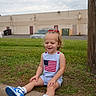 toddler, child, sitting, outdoor, grass, curb, sneakers, blue_shoes, american_flag, clothing, happy, smiling, shorts, hair_bow, red_bow, concrete, building, car, pole, daytime