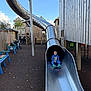 Kane is registered to the contest to win money with this photo: child, slide, playground, metal_slide, wooden_structure, bench, outdoor, daylight, blue_sky, person, play, casual_clothing, fun, recreation, activity, park, smiling, sitting, feet, happy