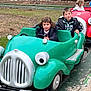 child, children, amusement_park, ride, toy_car, green_car, red_car, outdoor, track, trees, grass, jacket, happy, play, fun, person, pavement, daytime, smile, young