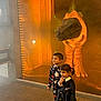 Kane is registered to the contest to win money with this photo: child, boy, girl, costume, halloween, dinosaur, display, fog, orange_light, indoor, smile, curious, floor, brick, exhibit, toy, fun, event, holiday, playful