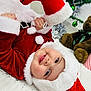 baby, child, santa_claus_costume, red_clothing, white_fur, smiling, face, teddy_bear, toy, holiday, christmas_tree, ornaments, blanket, indoor, floor, festive, cute, person, headwear, happy