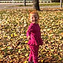 autumn, casual_wear, child, daylight, face, grass, happy, leaves, nature, outdoor, park, pink_clothing, playful, seasonal, smiling, sneakers, sunlight, toddler, tree, young_child