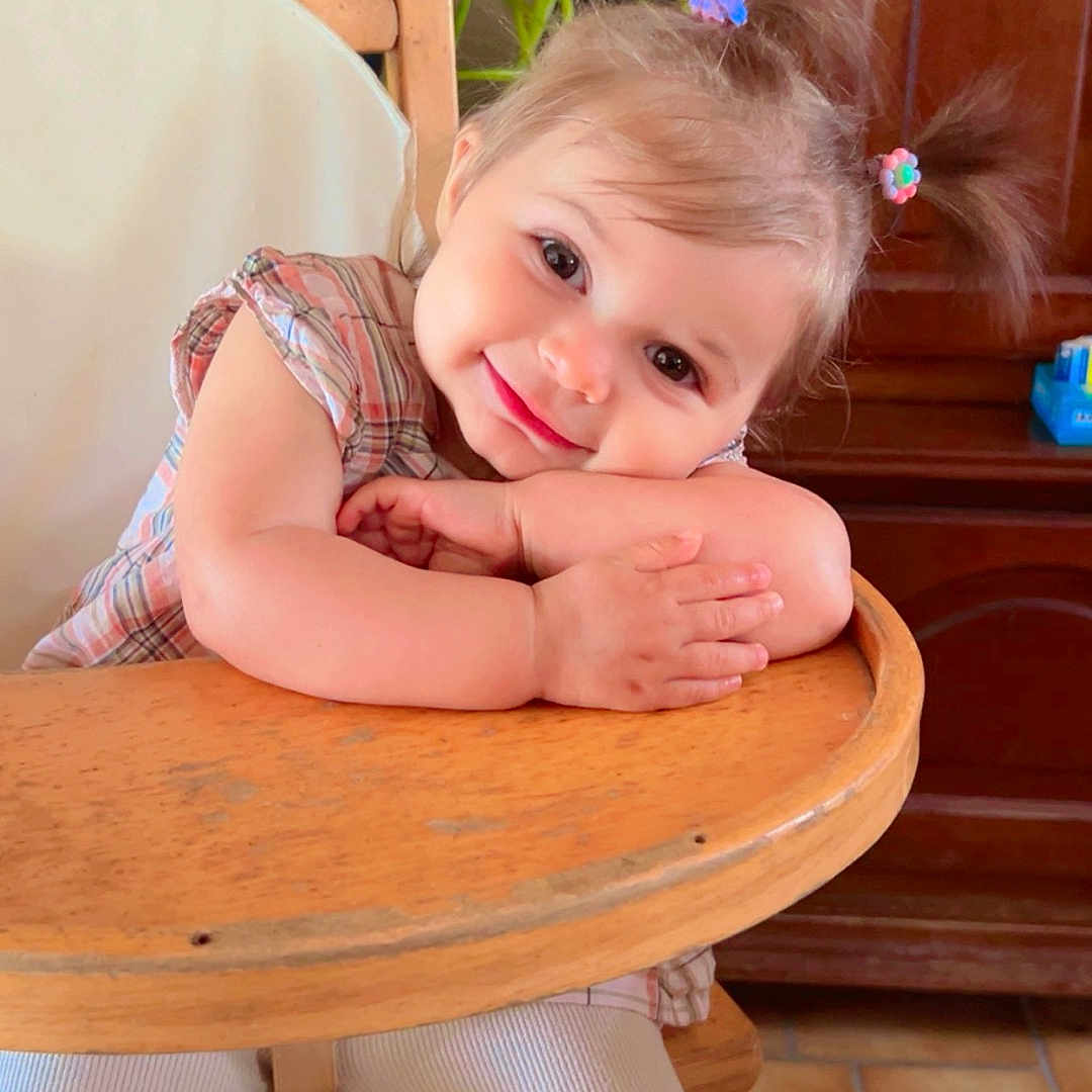 Mayhanna participe au concours pour gagner de l'argent avec cette photo : child, cozy, cute, face, floor_tiles, hair_clips, hands, happy, highchair, home, indoor, person, pigtails, plaid_shirt, plant, portrait, smiling, toddler, white_pants, wooden_furniture