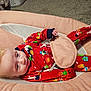 Freyja is registered to the contest to win money with this photo: baby, infant, pajamas, red_clothing, holiday_pattern, baby_seat, cushion, carpet, indoor, child, face, person, soft_texture, relaxed, wide_eyes, smile, hand, foot, sleepwear, cute