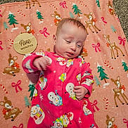 Freyja is registered to the contest to win money with this photo: baby, infant, pink_onesie, snowman_pattern, blanket, deer_pattern, wooden_plaque, five_months, carpet, milestone, cute, lying_down, indoors, holiday_theme, child, face, hand, clothing, soft_texture, portrait
