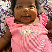 Storm joined the competition — help win amazing prizes! baby, infant, smile, pink_clothing, flower_embroidery, curly_hair, patterned_quilt, lying_down, happy, cute, child, closeup, portrait, indoor, skin, cheeks, person, apparel, fabric, baby_girl