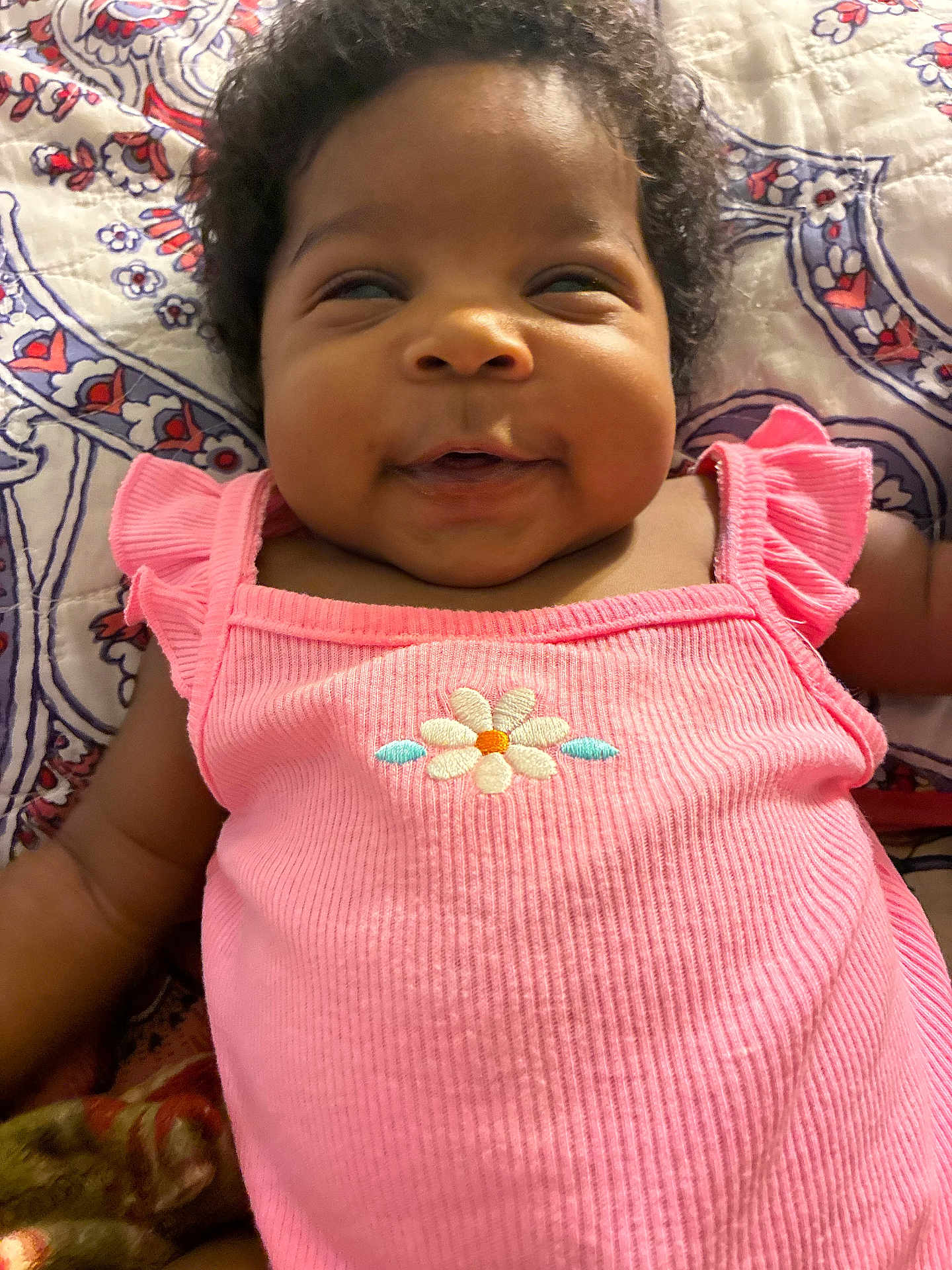 Storm joined the competition — help win amazing prizes! baby, infant, smile, pink_clothing, flower_embroidery, curly_hair, patterned_quilt, lying_down, happy, cute, child, closeup, portrait, indoor, skin, cheeks, person, apparel, fabric, baby_girl