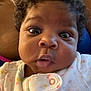 Storm is registered to the contest to win money with this photo: baby, face, curly_hair, onesie, polka_dots, closeup, chubby_cheeks, wide_eyes, infant, person, skin, mouth, nose, expression, child, portrait, indoor, human, cute, young