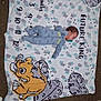 Xavier is registered to the contest to win money with this photo: baby, blanket, carpet, child, clothing, cartoon, floor, infant, laying_down, onesie, pacifier, person, plush, pattern, sleeping, soft, toy, young_child, animal_print, cute