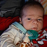 Xavier joined the competition — help win amazing prizes! baby, infant, pacifier, plush_toy, giraffe, hand, clothing, blanket, face, expression, indoors, cute, child, person, sleepwear, soft_toy, holding, portrait, newborn, resting