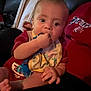 baby, child, pacifier, bib, red_shirt, hand, foot, person, indoor, couch, lap, face, skin, infant, sitting, comfort, chewing, toy, relaxed, dim_light