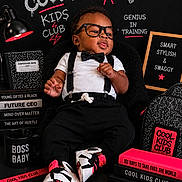 Mahari joined the competition — help win amazing prizes! baby, child, glasses, bow_tie, suspenders, sneakers, black_clothing, chalkboard, books, mug, backpack, pencil, lamp, composition_book, text, indoor, portrait, cute, smiling, props
