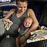 Waylon is registered to the contest to win money with this photo: baby, woman, smiling, indoor, blanket, couch, striped_clothing, yellow_socks, holding, tattoo, remote_control, pacifier, home, comfort, happy, portrait, infant, casual, relaxed, family