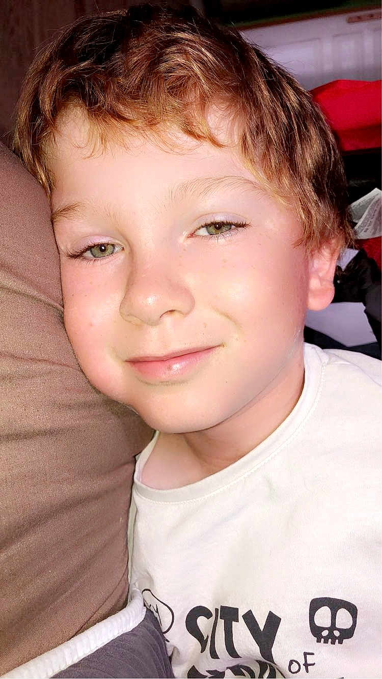 Hugo participe au concours pour gagner de l'argent avec cette photo : child, smiling, close_up, face, green_eyes, light_brown_hair, tshirt, skull_graphic, cushion, indoor, portrait, casual, young, happy, resting, comfortable, person, skin, head, expression