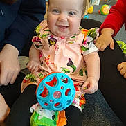 Skyla-Jayne joined the competition — help win amazing prizes! baby, child, smiling, toy, ball, floral_dress, indoor, carpet, happy, person, hand, play, colorful, legs, sitting, cute, infant, people, floor, casual