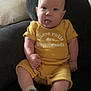 baby, child, infant, yellow_outfit, sitting, tongue_out, chair, cushion, sock, shoe, plush, cute, indoor, portrait, smiling, skin, head, expression, cozy, homedecor