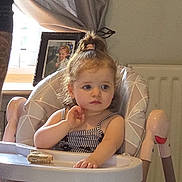 Amelia Grace is registered to the contest to win money with this photo: toddler, child, high_chair, sandwich, indoor, curtains, window, portrait, person, hair_tie, photo_frame, radiator, clothing, furniture, expression, table, seat, skin, face, home